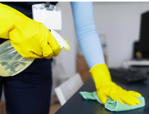 Hands in yellow gloves applying a spray and wiping a surface.